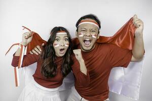 A young Asian couple with a happy successful expression wearing red top and headband while holding Indonesia's flag, isolated by white background. Indonesia's independence day concept. photo