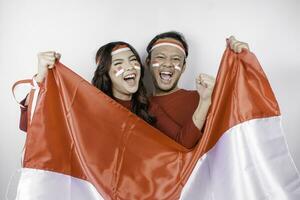 A young Asian couple with a happy successful expression wearing red top and headband while holding Indonesia's flag, isolated by white background. Indonesia's independence day concept. photo