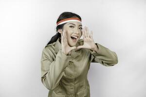 Young beautiful civil worker woman is wearing indonesia's flag headband and shouting or yelling isolated by a white background. Communication and independence day concept photo