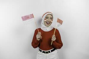 Happy smiling Indonesian muslim woman wearing red top and white hijab holding Indonesia's flag to celebrate Indonesia Independence Day. Isolated by white background. photo