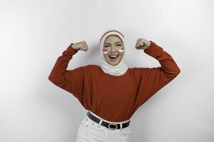 Excited Asian muslim woman wearing a red top and white hijab showing strong gesture by lifting her arms and muscles smiling proudly. Indonesia's independence day concept. photo