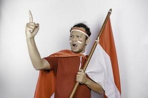 An enlighten young Asian man is wearing red t-shirt and holding Indonesia's flag looks inspired by ideas, isolated by white background photo