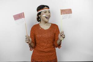 Happy smiling Indonesian woman wearing red kebaya and headband holding Indonesia's flag to celebrate Indonesia Independence Day isolated over white background. photo