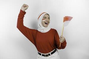 A young Asian muslim woman with a happy successful expression wearing red top and white hijab while holding Indonesia's flag, isolated by white background. Indonesia's independence day concept. photo