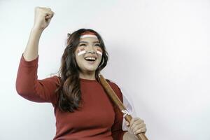 A young Asian woman with a happy successful expression wearing red top and headband while holding Indonesia's flag, isolated by white background. Indonesia's independence day concept. photo