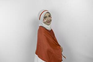 Happy smiling Indonesian muslim woman wearing red top and white hijab holding Indonesia's flag to celebrate Indonesia Independence Day. Isolated by white background. photo
