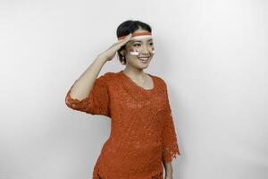 Beautiful Asian woman wearing red kebaya and flag headband giving salute celebrate Indonesian independence day on August 17 isolated over white background photo