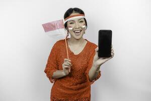 A portrait of a smiling Asian woman wearing red kebaya and headband and showing her phone, isolated by white background. Indonesia's independence day concept photo