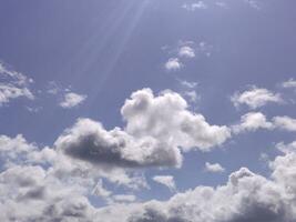 White clouds and sun rays over blue sky background. Fluffy cumulus clouds shapes photo