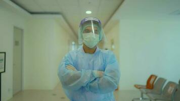 Porträt von ein Krankenschwester Mann mit gekreuzt Waffen tragen ein Gesicht Maske und Putten auf ein Gesicht Schild suchen beim das Kamera im ein Krankenhaus medizinisch Konzept. video