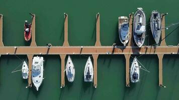 Sailboats moored in port with green water on sunny day. Top aerial view video