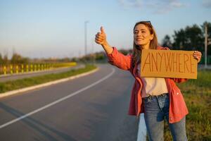 Woman is hitchhiking on roadside trying to stop car. She is holding cardboard with inscription. photo