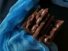 Pieces of chocolate with nuts and raisins on a dark background photo