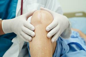 Doctor checking Asian elderly woman patient with scar knee replacement surgery in hospital. photo