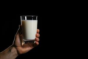 Hand holding a glass of fresh milk isolated on black background with copy space. ai generated photo