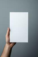 A human hand holding a blank sheet of white paper or card isolated on grey background. ai generated photo