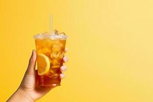A hand holding takeaway plastic cup of delicious iced lemon tea isolated on yellow background with copy space. ai generated photo