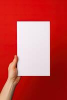 A human hand holding a blank sheet of white paper or card isolated on red background. ai generated photo