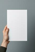 A human hand holding a blank sheet of white paper or card isolated on grey background. ai generated photo