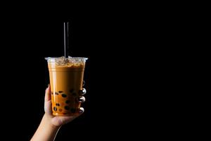 A hand holding takeaway plastic cup of delicious iced bubble milk tea and black pearls isolated on black background with copy space. ai generated photo