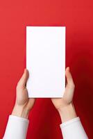 A human hand holding a blank sheet of white paper or card isolated on red background. ai generated photo