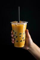 A hand holding takeaway plastic cup of delicious iced bubble milk tea and black pearls isolated on black background. ai generated photo