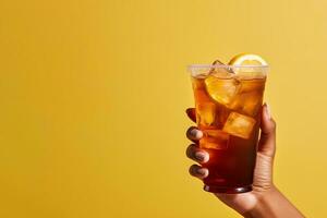 A hand holding takeaway plastic cup of delicious iced lemon tea isolated on yellow background with copy space. ai generated photo