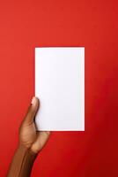 A human hand holding a blank sheet of white paper or card isolated on red background. ai generated photo