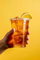 A hand holding takeaway plastic cup of delicious iced lemon tea isolated on yellow background. ai generated photo