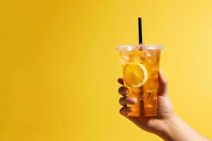 un mano participación para llevar el plastico taza de delicioso con hielo limón té aislado en amarillo antecedentes con Copiar espacio. ai generado foto