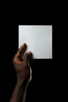 A human hand holding a blank sheet of white paper or card isolated on black background. ai generated photo