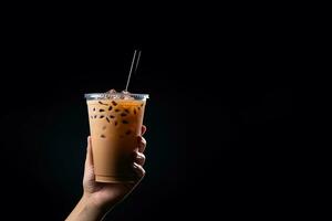 A hand holding takeaway plastic cup of delicious iced bubble milk tea and black pearls isolated on black background with copy space. ai generated photo