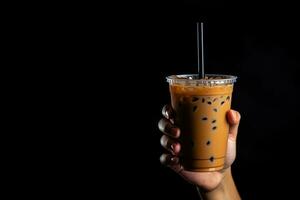 A hand holding takeaway plastic cup of delicious iced bubble milk tea and black pearls isolated on black background with copy space. ai generated photo