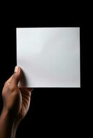 A human hand holding a blank sheet of white paper or card isolated on black background. ai generated photo