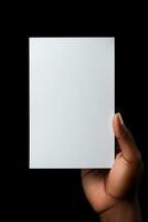 A human hand holding a blank sheet of white paper or card isolated on black background. ai generated photo