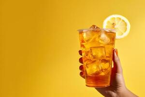 A hand holding takeaway plastic cup of delicious iced lemon tea isolated on yellow background with copy space. ai generated photo