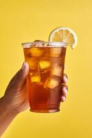 A hand holding takeaway plastic cup of delicious iced lemon tea isolated on yellow background. ai generated photo