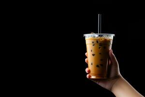 A hand holding takeaway plastic cup of delicious iced bubble milk tea and black pearls isolated on black background with copy space. ai generated photo