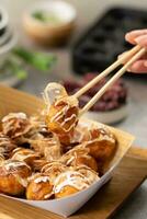 a person holding chopsticks over a tray of Takoyaki photo