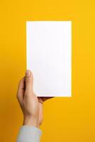 A human hand holding a blank sheet of white paper or card isolated on yellow background. ai generated photo