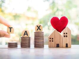 Close up hand holding wooden block with word TAX on stack of coins. The concept of paying tax for house and property. photo