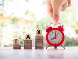 Close up hand holding red alarm and wooden blocks with the word TAX on stack of coins. The concept of paying tax for everything. photo