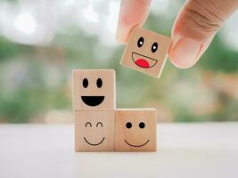 Close up hand holding happy face wooden block. Customer service rating experience, feedback emotion and satisfaction survey. photo