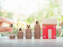 Close up hand holding wooden block with word SAVE, miniature house, stack of coins for Investment property concept. Saving money for buy a house. photo