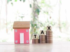 Miniature house and wooden blocks with the word TAX on stack of coins. The concept of paying tax for house and property. Property taxes. photo