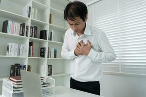 mano sostener cofre con corazón ataque síntomas, asiático hombre trabajando difícil tener cofre dolor causado por corazón enfermedad, filtración, dilatación, engrandecido coronario corazón, prensa en el cofre con un doloroso expresión foto