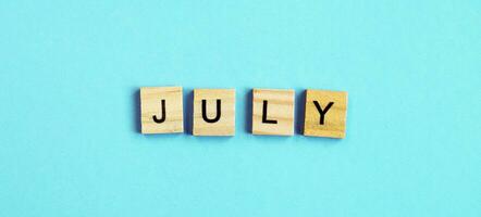 July word made by wooden cubes on a blue turquoise background photo