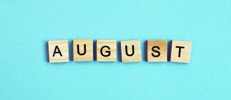 August word made by wooden cubes on a blue turquoise background. photo