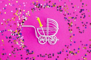 One year birthday.baby stroller with candle in form of the number one on a pink background with stars confetti sequins photo