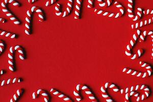 Flat lay Christmas composition with frame of candy canes on a red background. Copy space for text photo
